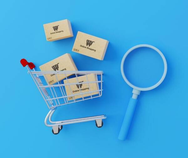 A small shopping cart filled with boxes that say online shopping, next to a large magnifying glass