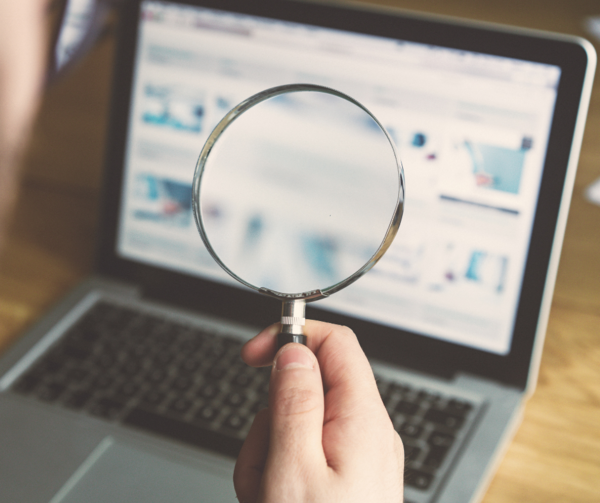 a hand holding a magnifying glass over the top of a laptop computer screen